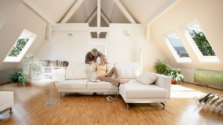 een echtpaar wordt getoond op hun zolderappartement in de woonkamer, de dakramen aan de zijkanten zijn open voor ventilatie