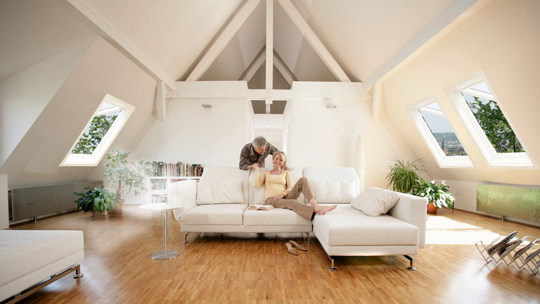 een echtpaar wordt getoond op hun zolderappartement in de woonkamer, de dakramen aan de zijkanten zijn open voor ventilatie