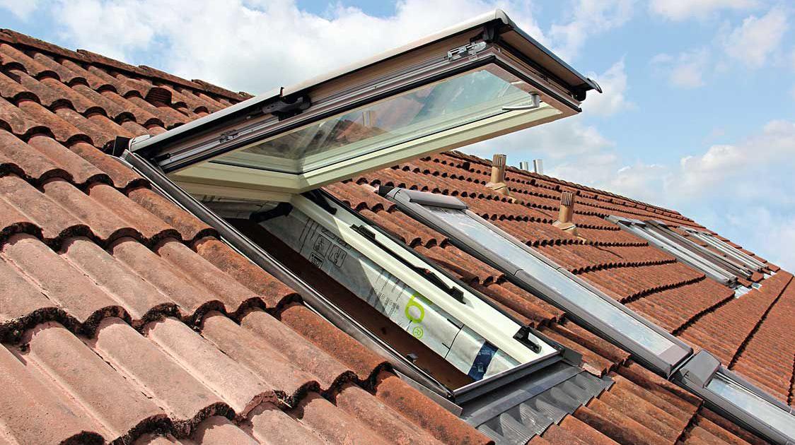 Een open Designo R8-draaiventilraam op een dak met verder gesloten dakramen